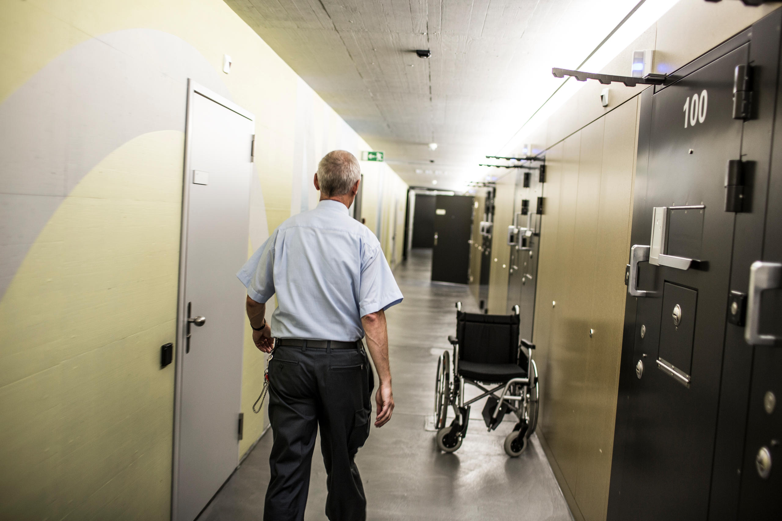 Un guardia camina por el corredor de una prisión. En el corredor hay una silla de ruedas
