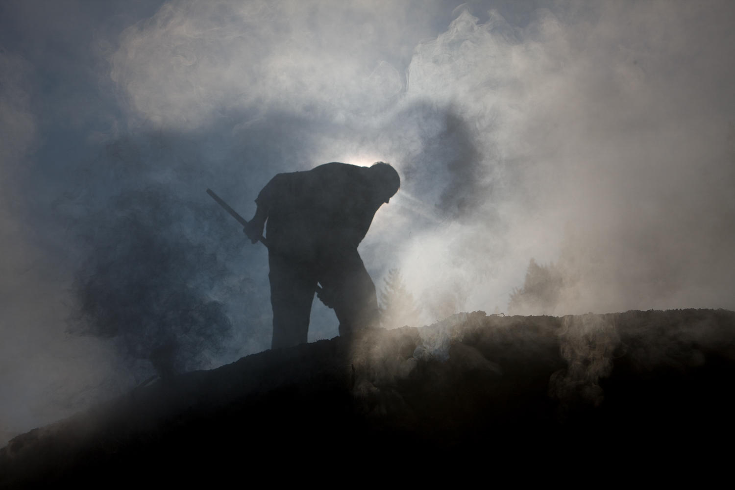 Entre el humo se advierta la silueta de un hombre removiendo las brasas.