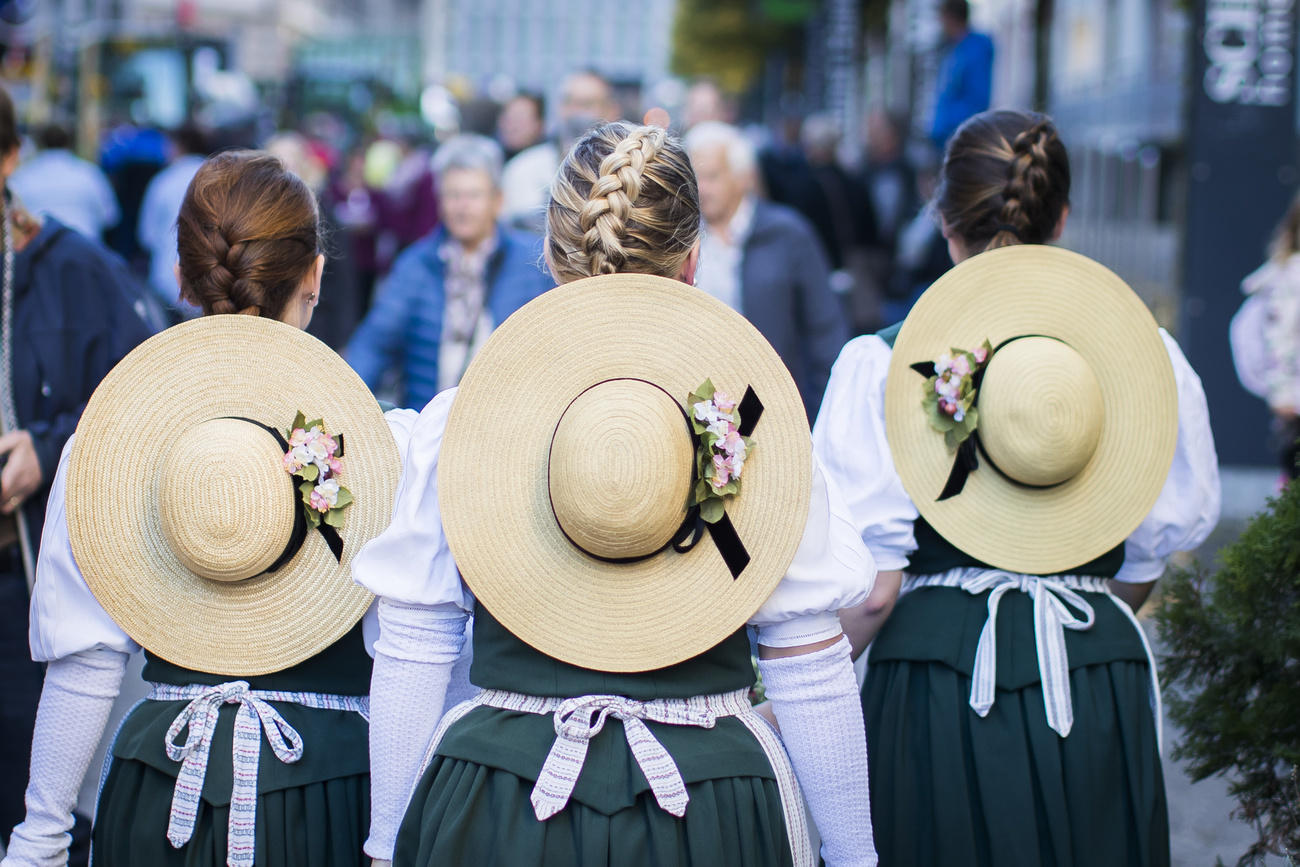 Tre contadine in costume tradizionale, viste di schiena durante quella che appare come una manifestazione folcloristica