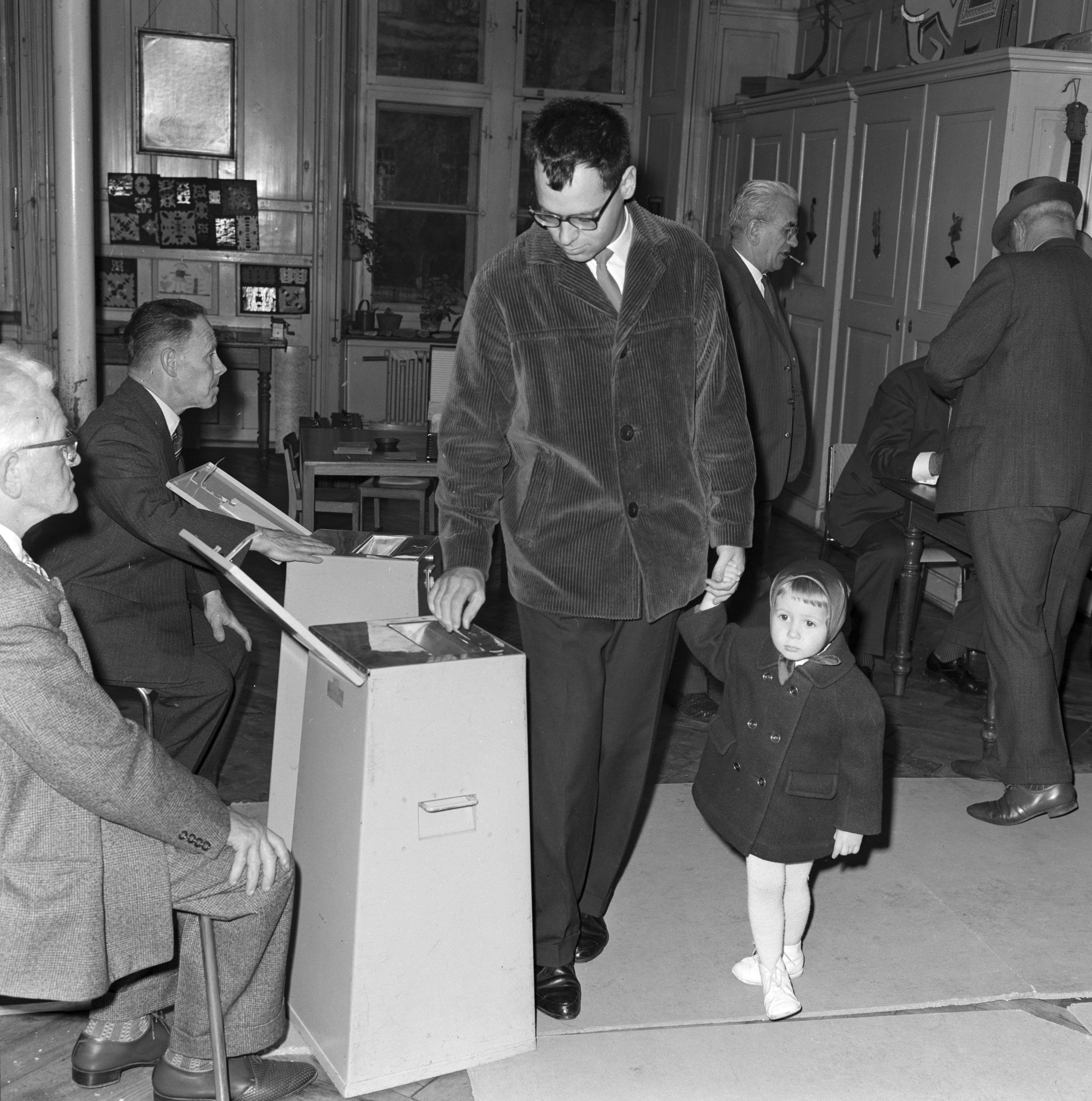 Homme avec un petit enfant devant une urne de vote.