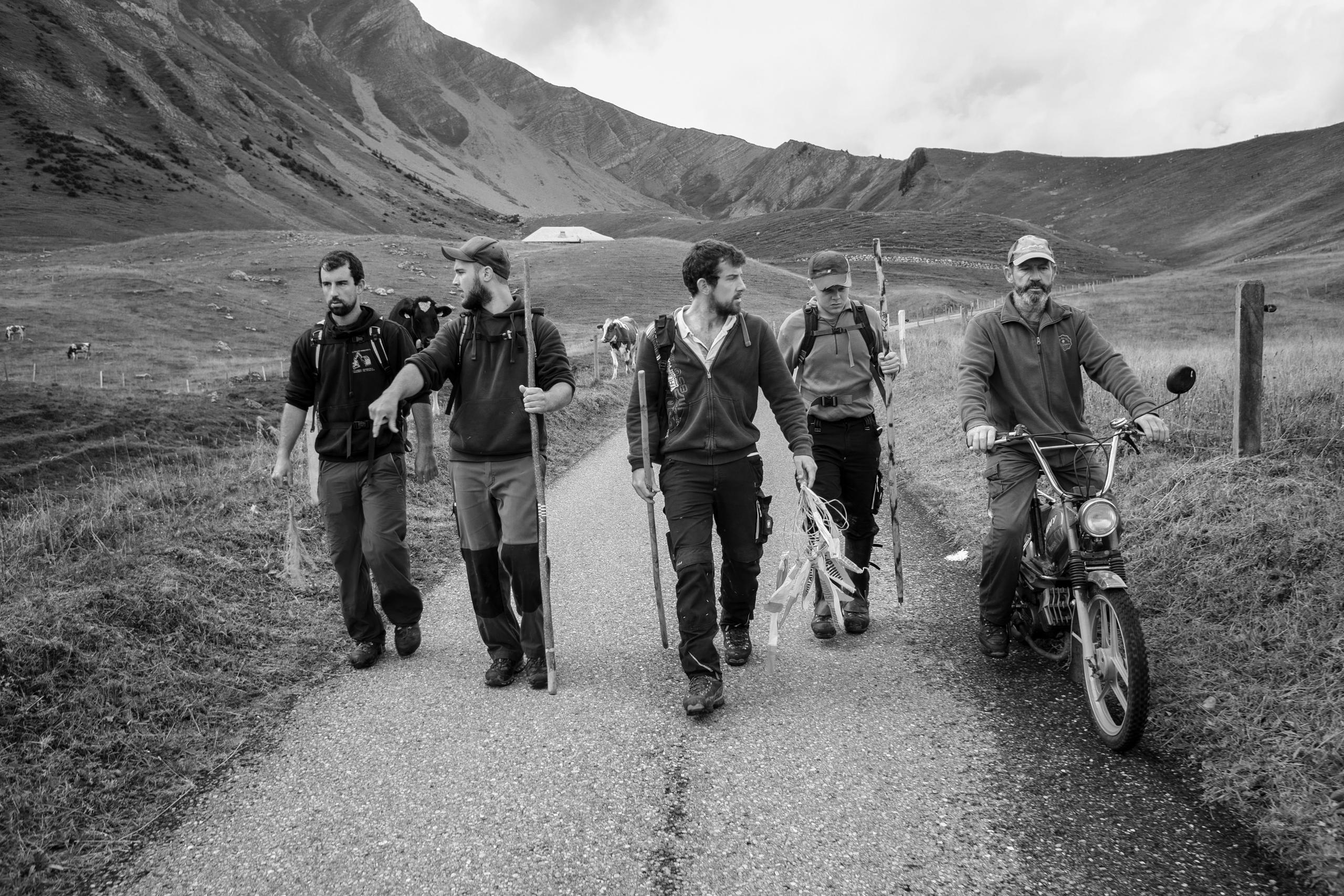 men walking on a road, one on a moped