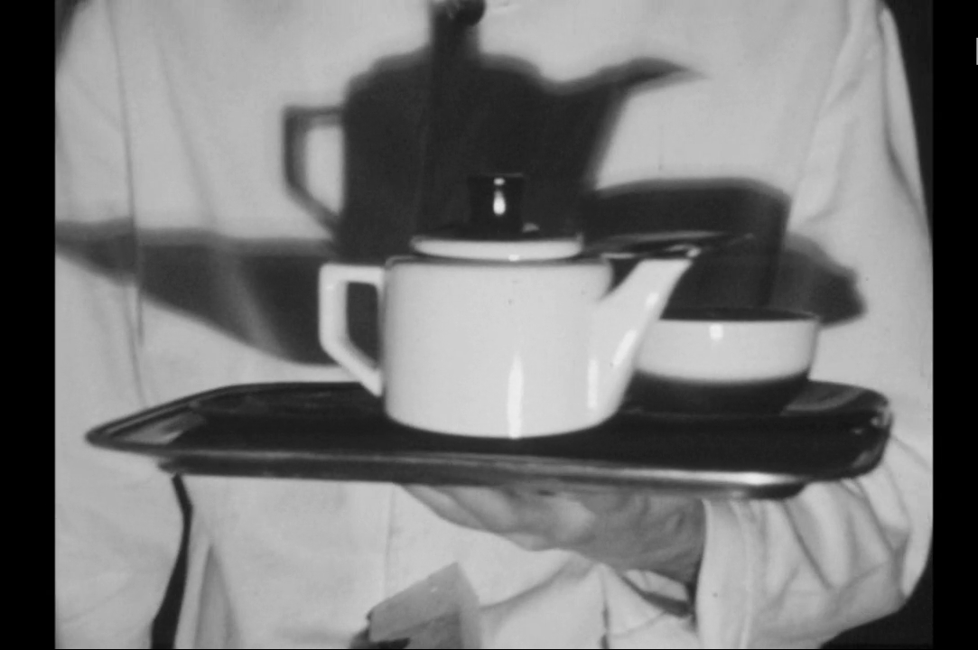 Primo piano di un vassoio con teiera e tazza, retto da un cameriere vestito di bianco