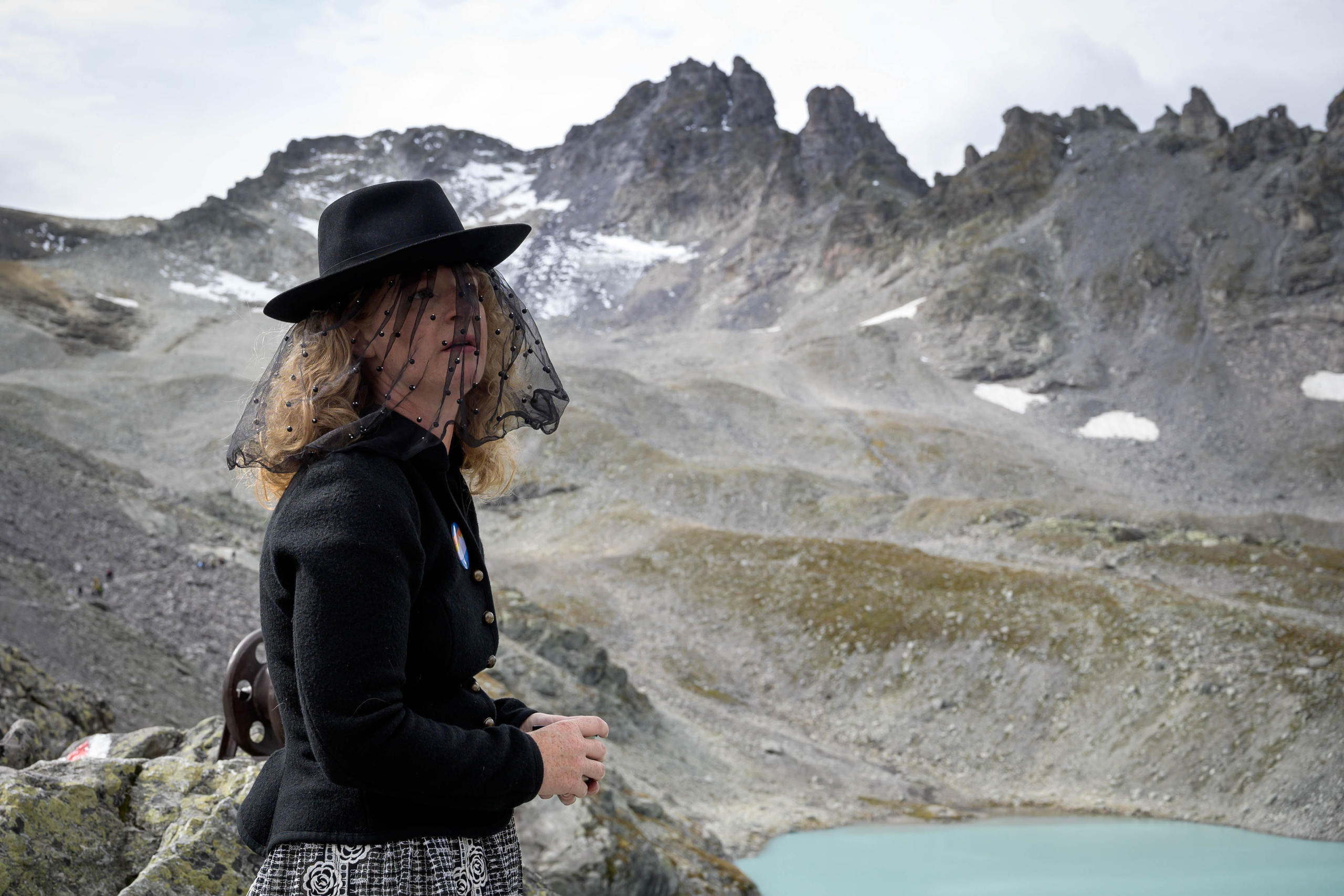 Una donna vestita a lutto su una montagna in cui si vedono dei resti di quello che un tempo era un ghiacciaio.