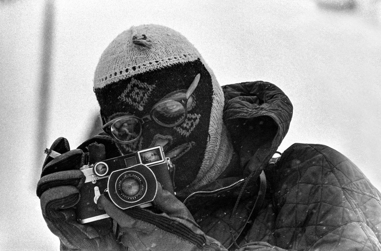 un uomo con un passamontagna tiene in mano una macchina fotografica e una sigaretta