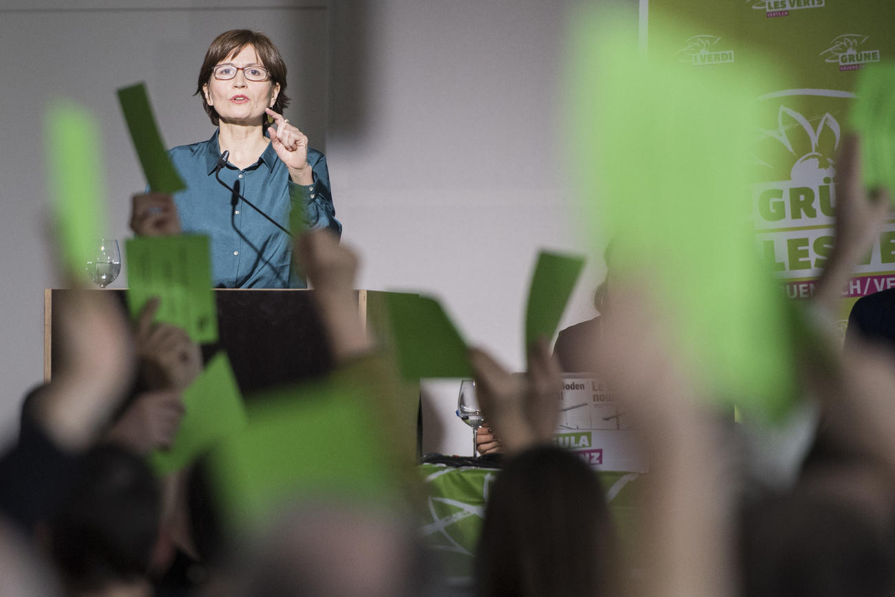 Mujer en una tribuna rodeada de gente con tarjetas verdes en la mano