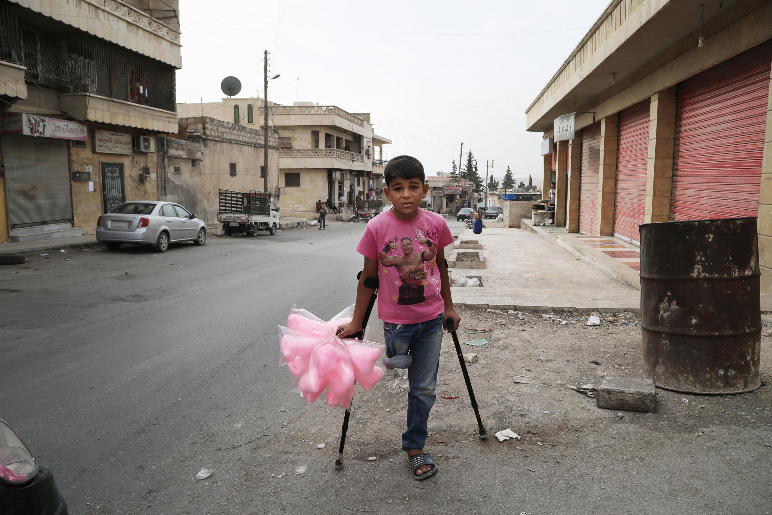 Boy in pink t-shirt stands on crutches with bags of cotton candy in his one hand