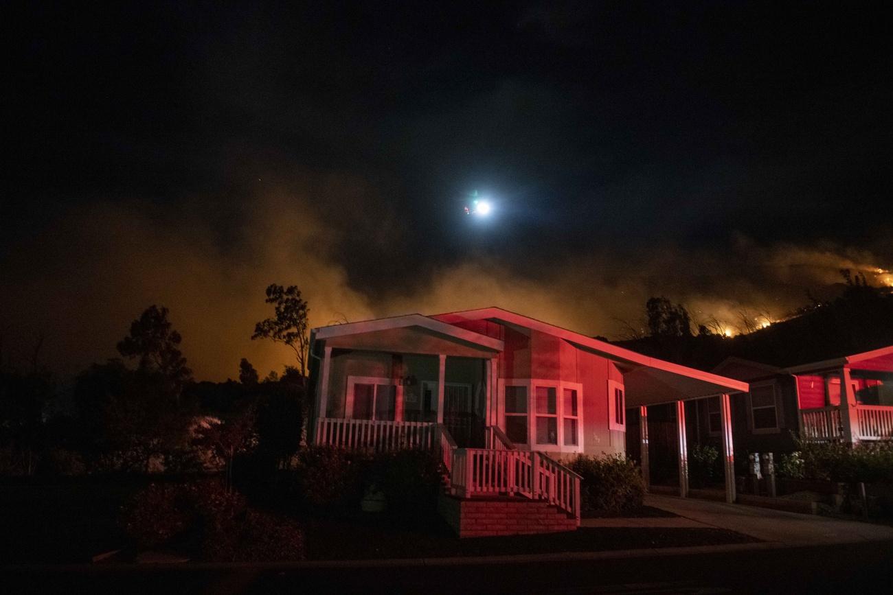 Immagine di una casa al buio ai margini di un bosco, sul fondo s intravvede un incendio