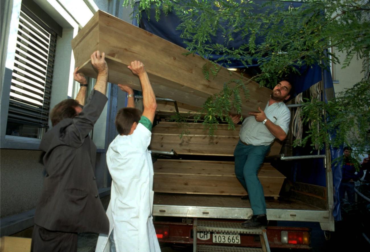 Tres hombres cargan ataudes.