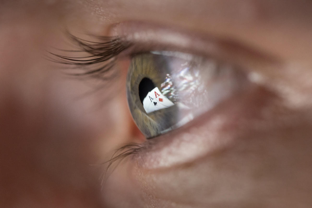 Black ace of clubs and red ace of diamonds reflect in a man s pupil.