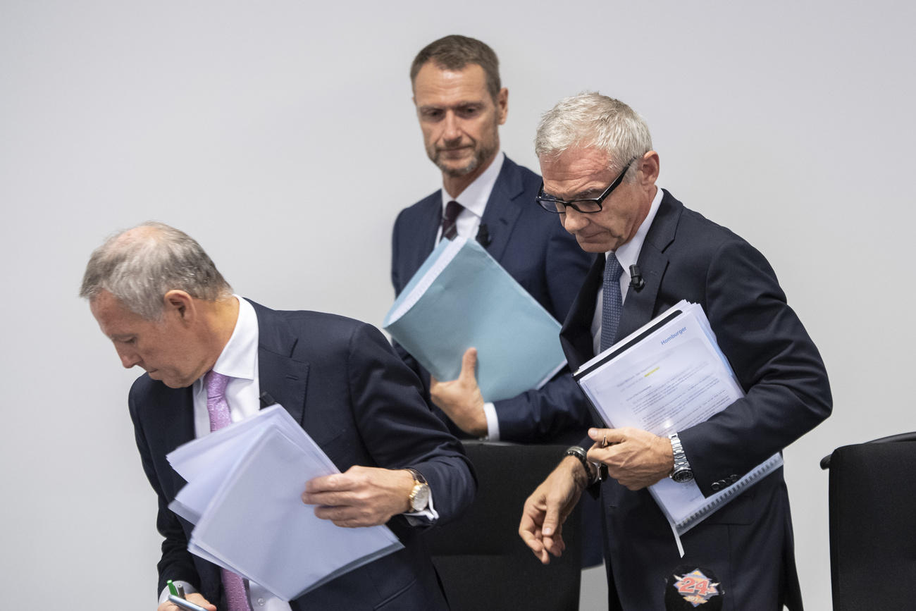 three men in suits looking down and papers under the arms