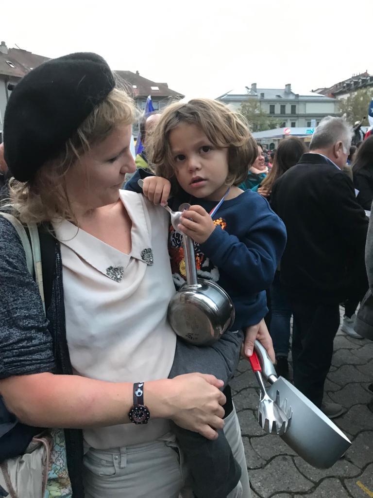 Una mujer con su hijo en brazos. Ambos llevan cacerolas