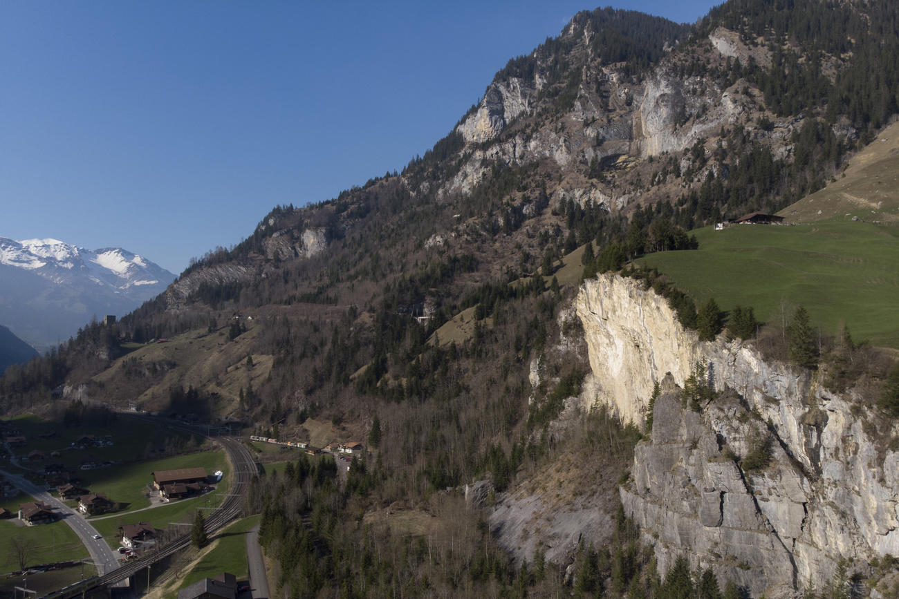 Veduta aerea di una frana sovrastata da un prato; strade e case a valle