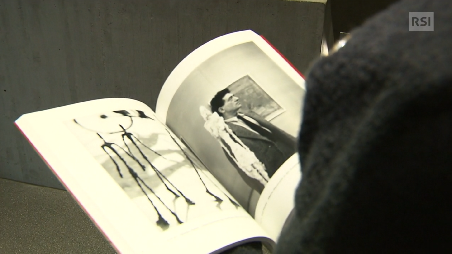 Uoo di schiena sfoglia un catalogo con fotografie; in una si vede l artista Alberto Giacometti
