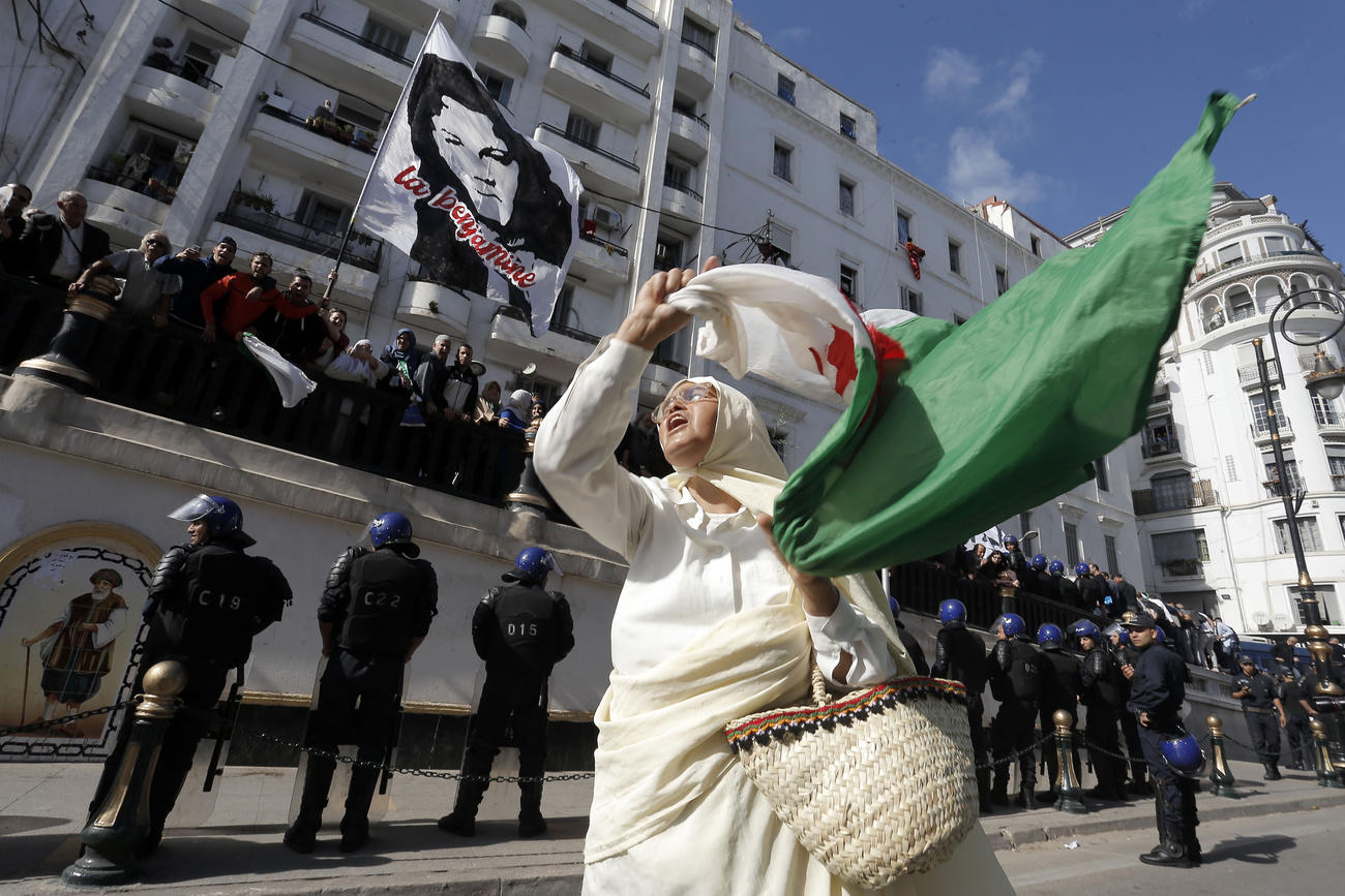 سيدة جزائرية بلباس تقليدي تلوح بعلم بلادها امام قوات الشرطة