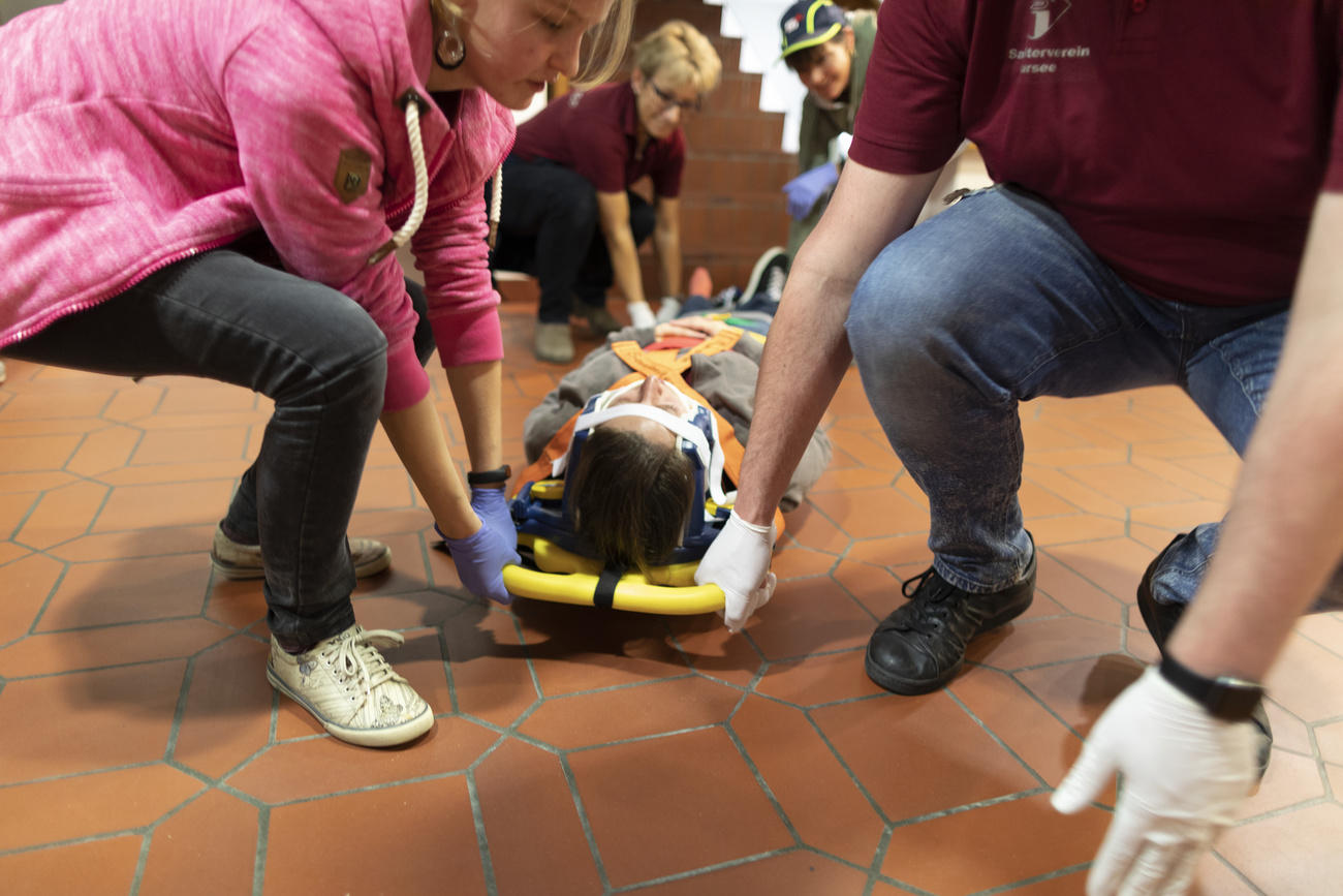 Quattro persone, non vestite da personale paramedico, sollevano una barella sulla quale è stata assicurata una donna