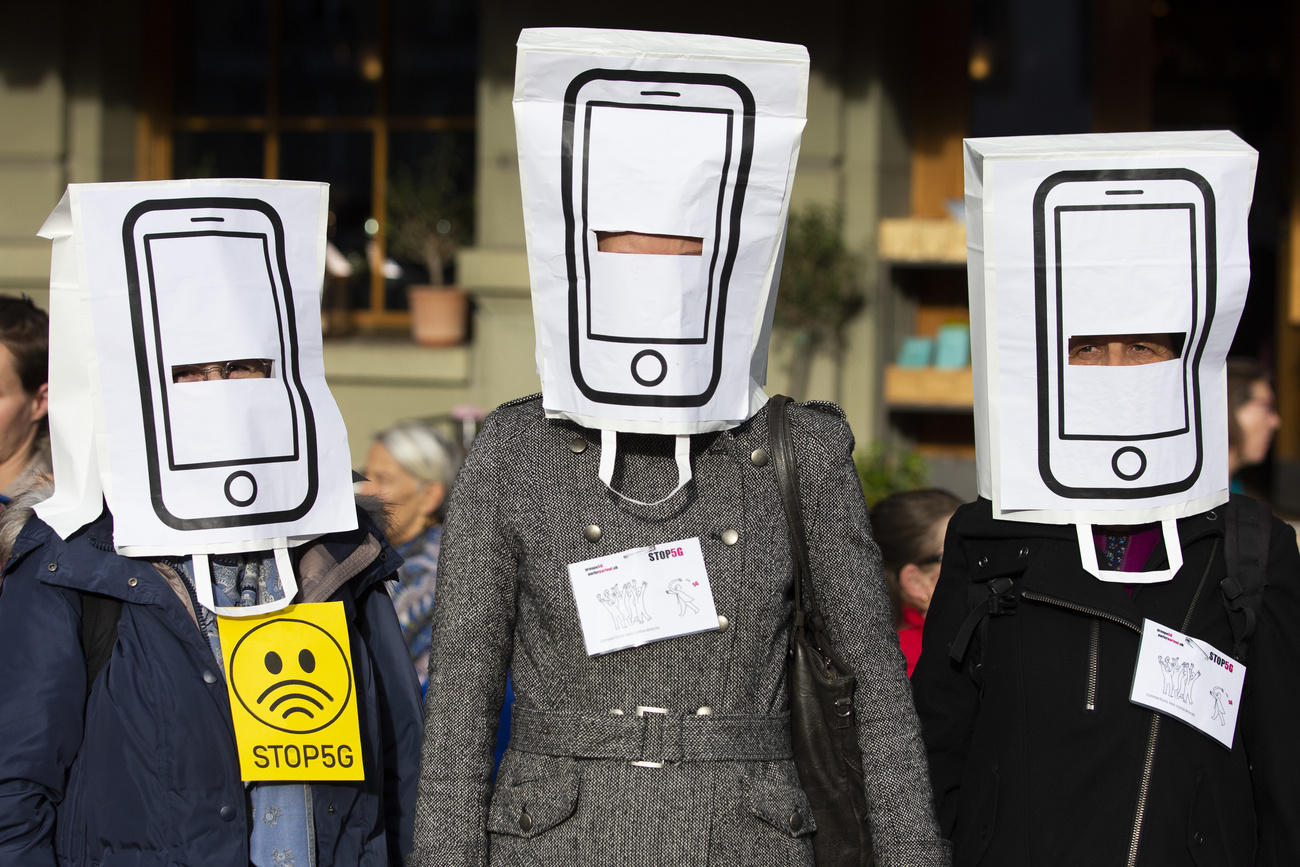 Tre persone indossano sulla testa un sacchetto di carte rovesciato con l effigie di un telefonino; attorno, manifestanti
