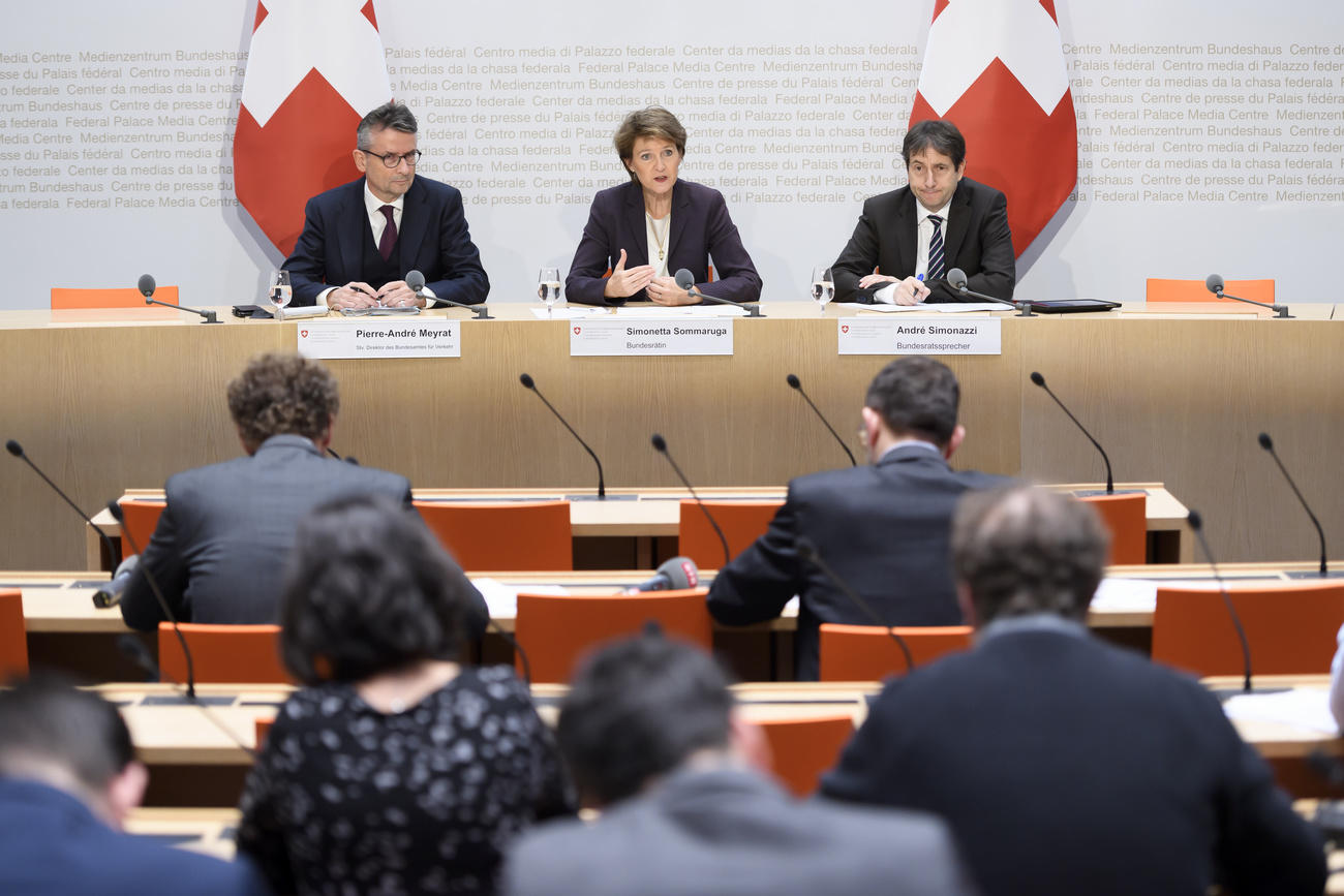 Sala conferenze; giornalisti, seduti, di schiena; al tavolo, in lontananza, Sommaruga con due collaboratori