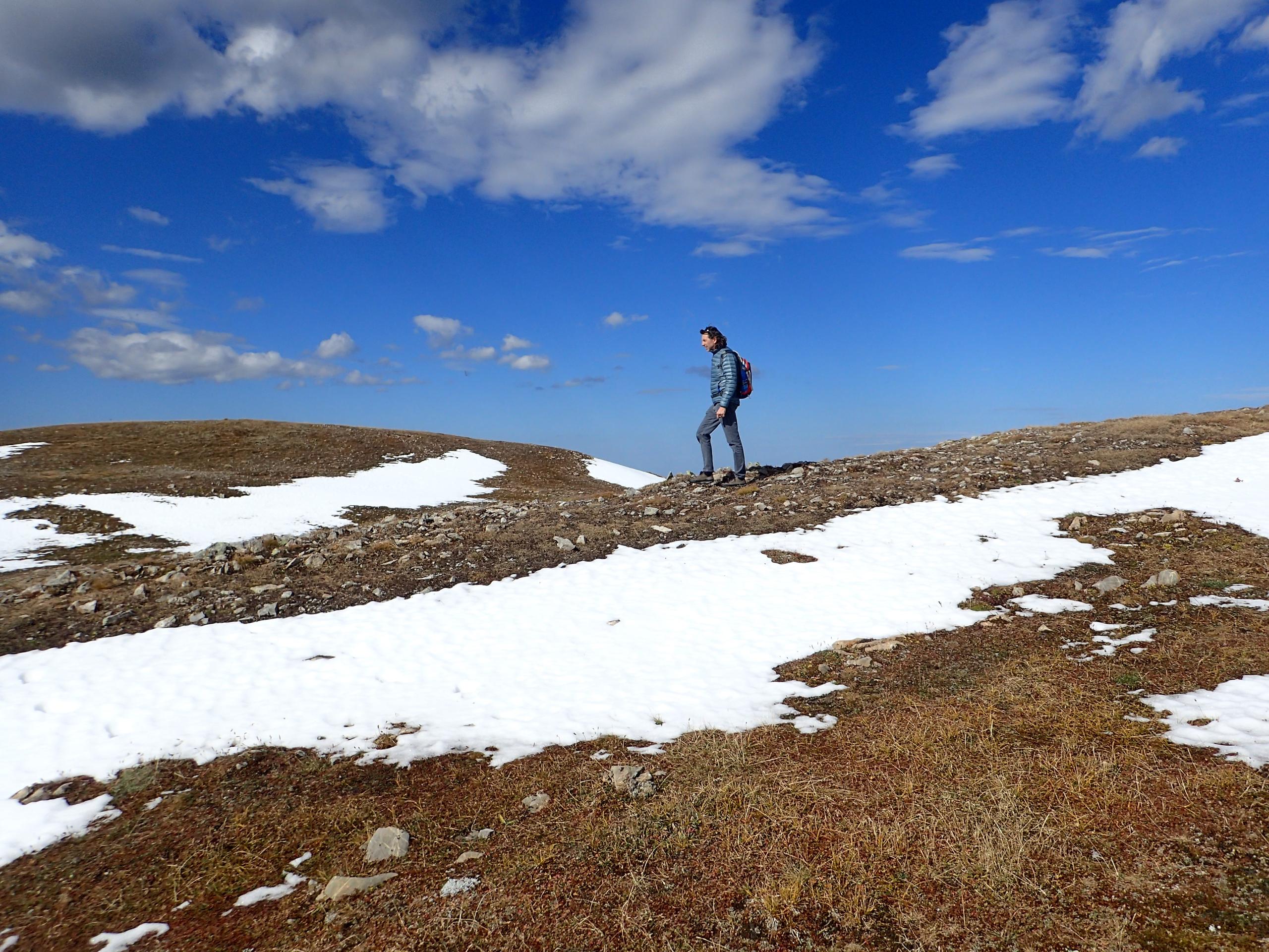 Man walking along mountain ridge, amid rock and snow patches