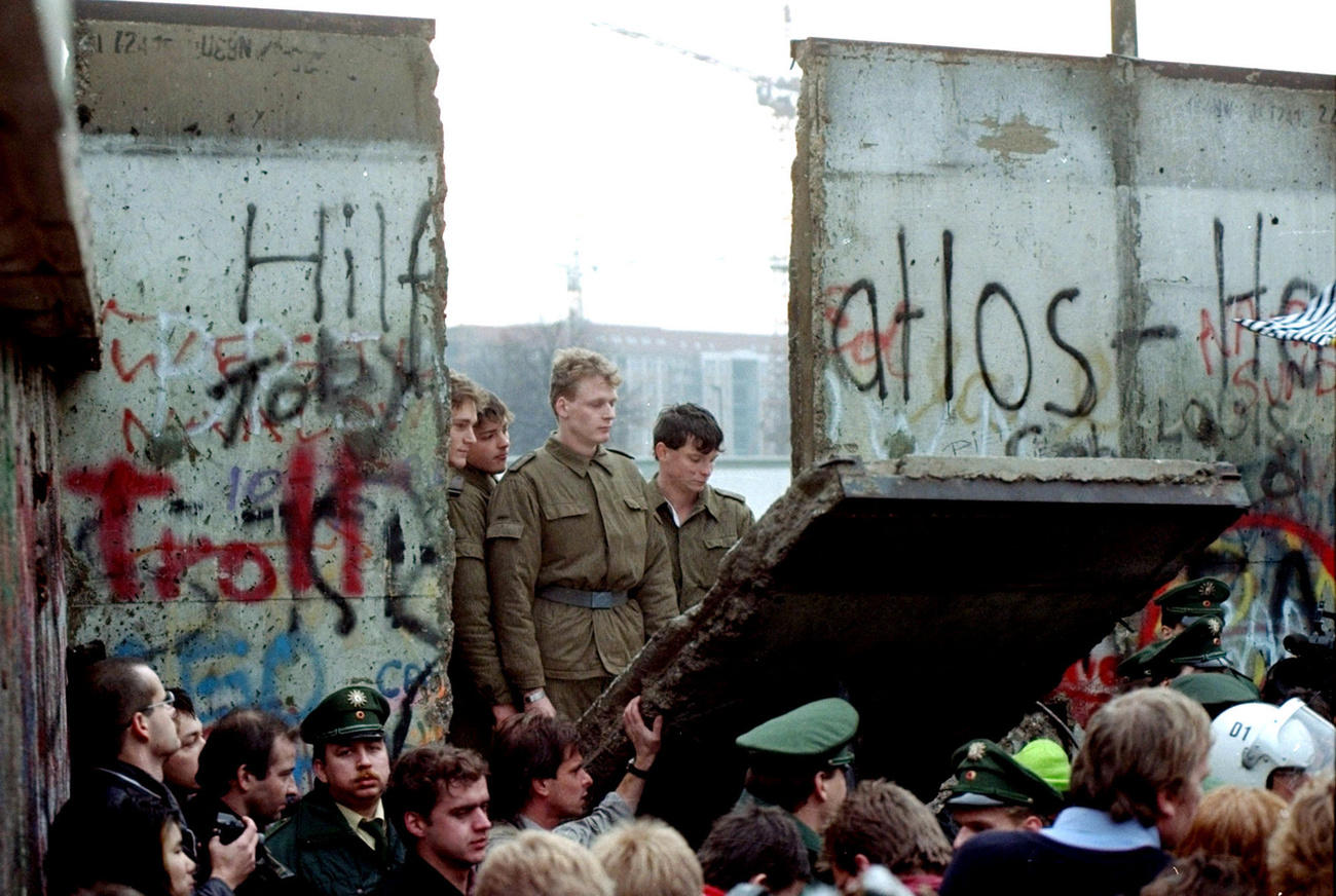 Des soldats regardent à travers un brèche du Mur de Berlin.