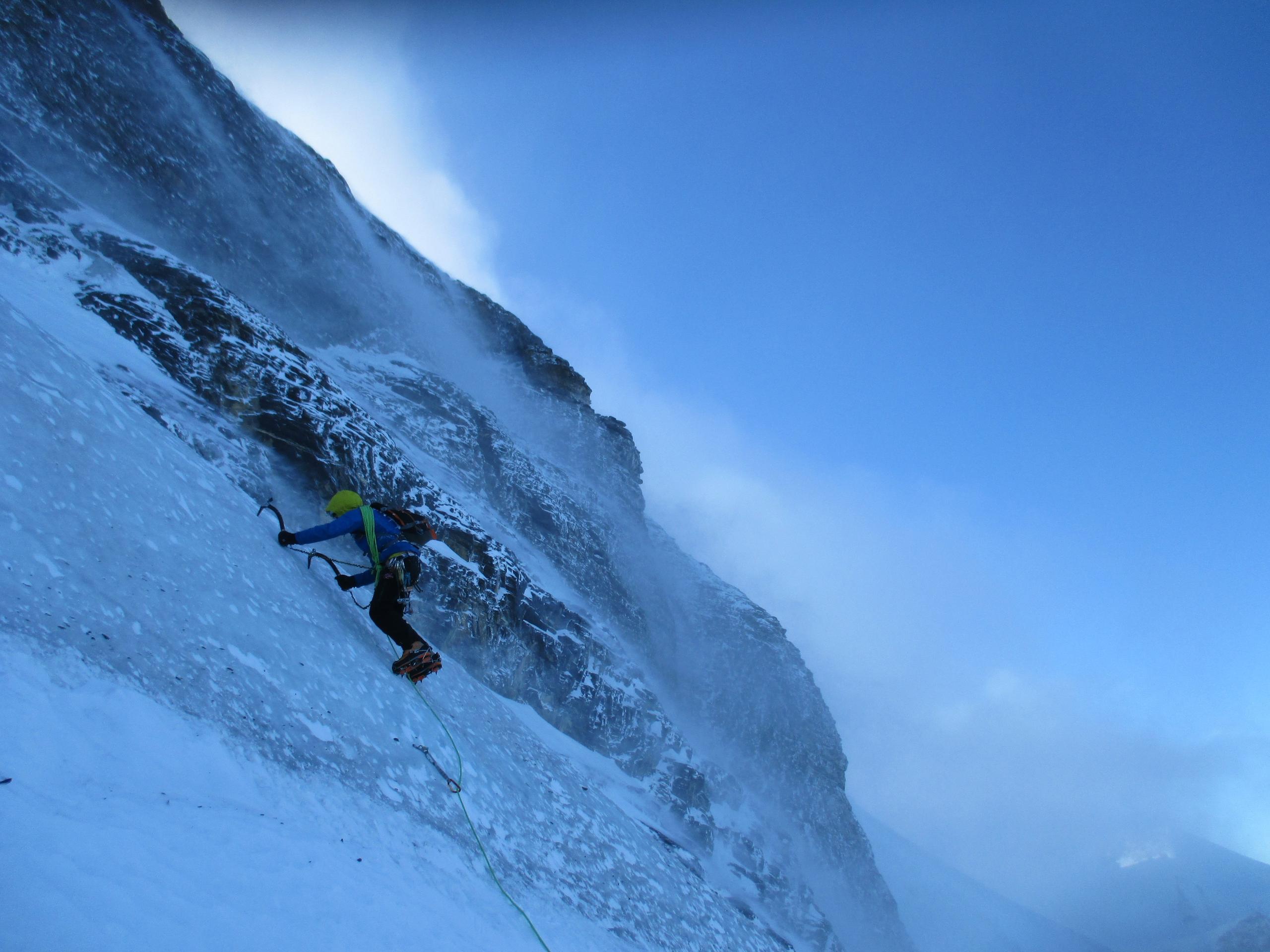 Climber on icy mountain face, climbing with two ice axes