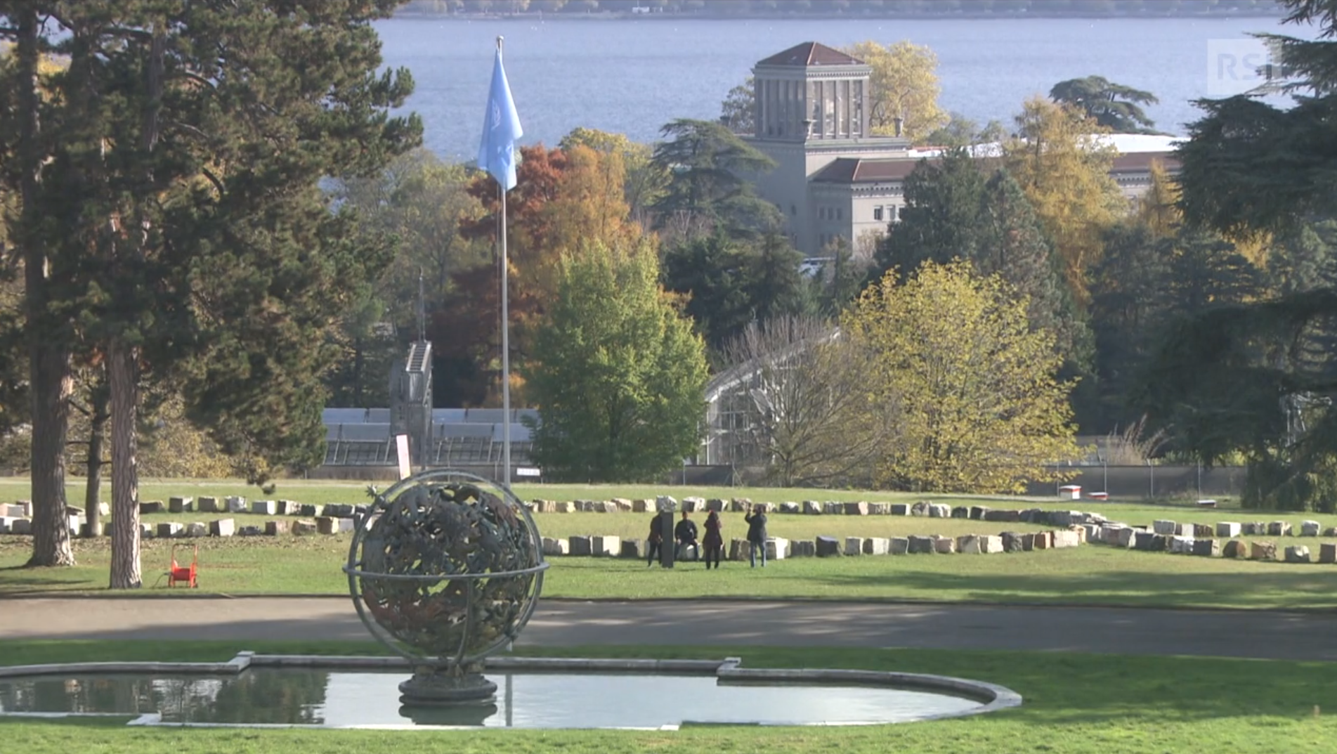 Veduta di un parco in riva al lago con grandi edifici, una bandiera dell Onu e la scultura di un globo