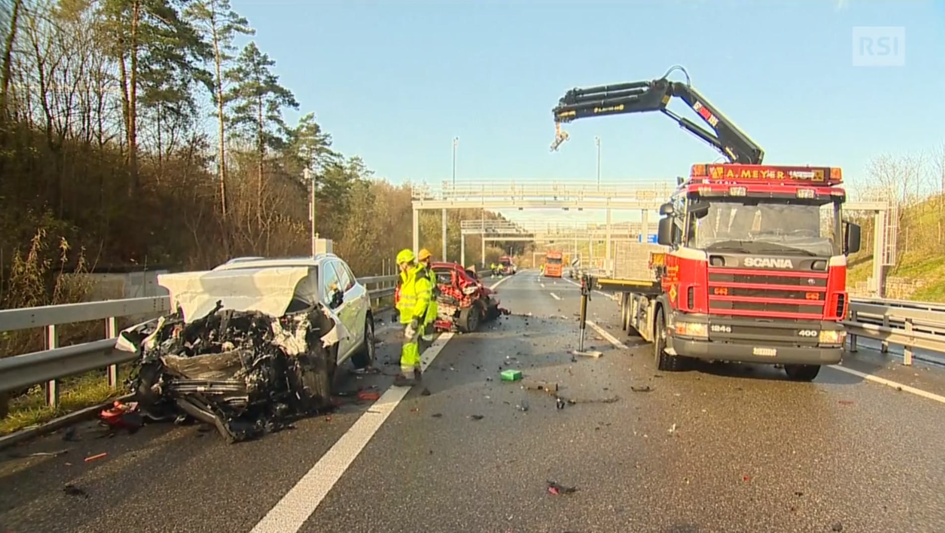 Due auto gravemente danneggiate al bordo di un autostrada; camion con gru sta per caricare un relitto