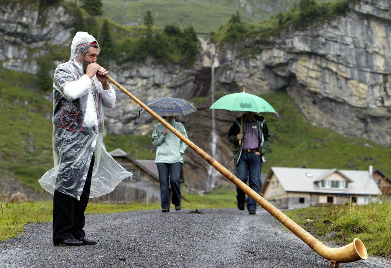 Bajo la lluvia, un hombre toca un cuerno de los Alpes