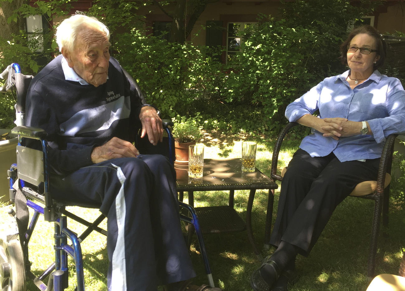 David Goodall con una enfermera. Ambos están sentados en un jardín.