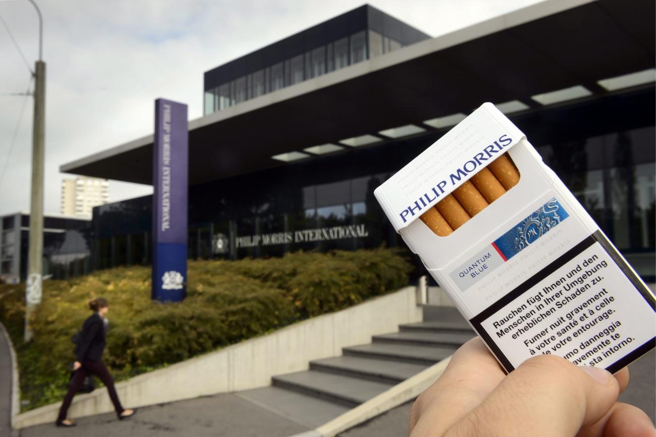 Hand holds cigarette packet in from of Philip Morris building