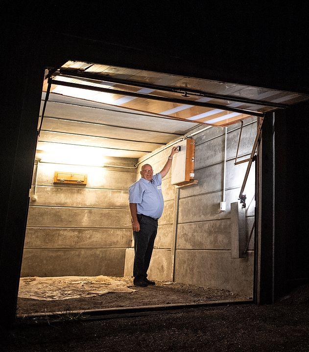 Ein Mann steht in einer Garage mit offenem Tor, draussen ist es Nacht.