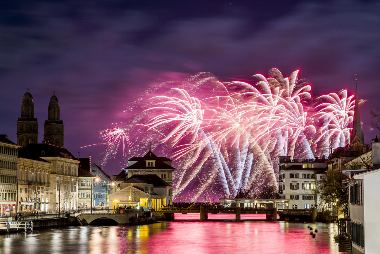 Immagine di Zurigo di notte con facciate delle case illuminate, scattata dal fiume, e fuochi d artificio in lontananza