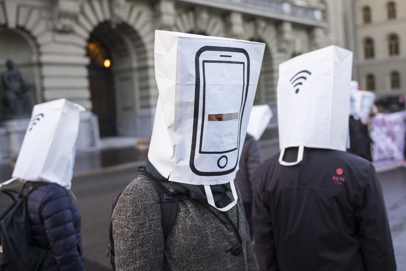Manifestantes encapuchados con bolsas de papel en forma de teléfonos