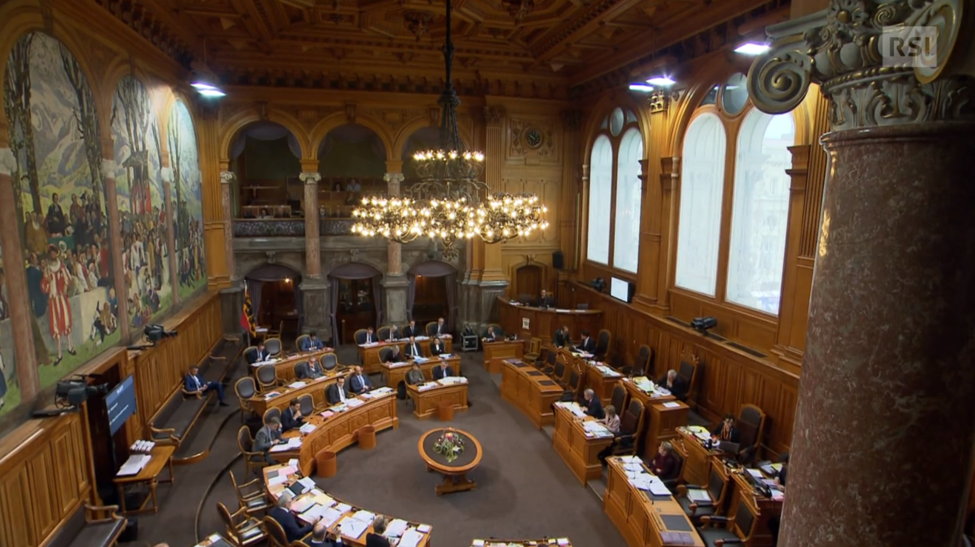 Una sala parlamentare con estesi dipinti e grande lampadario vista dall alto.
