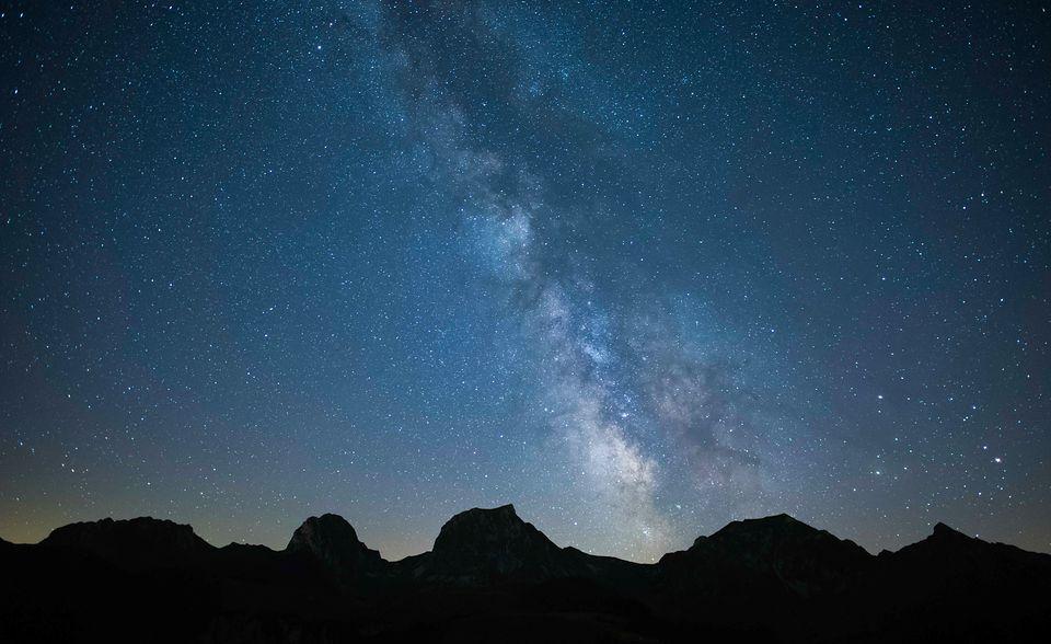 Nachthimmel mit einer Milchstrasse, im Hintergrund eine Bergkette.