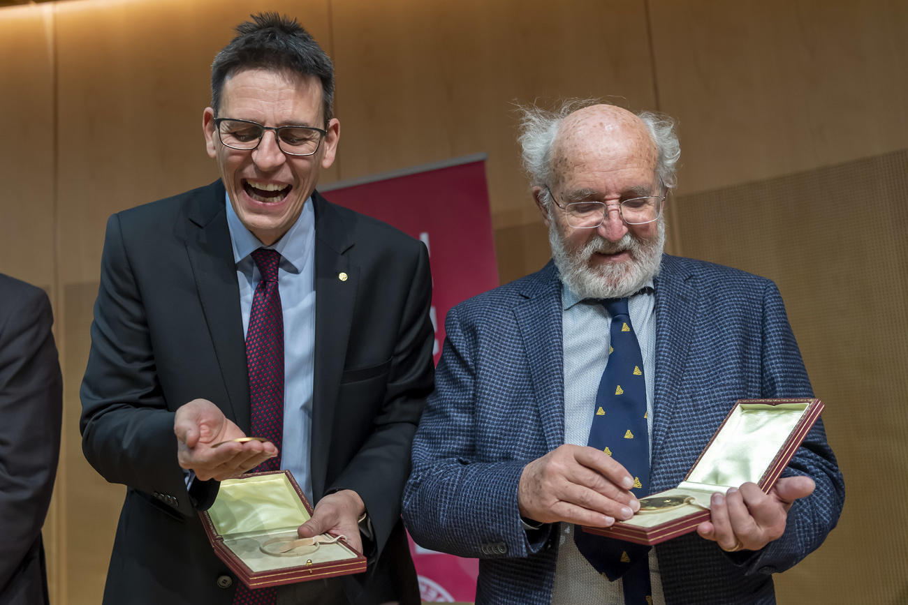 「たまらないな！」とでも言っているかのよう。昨年12月14日、スウェーデンのストックホルムで、取材陣に対しノーベル賞のメダルを見せるディディエ・ケロー氏（写真左）とミシェル・マイヨール氏