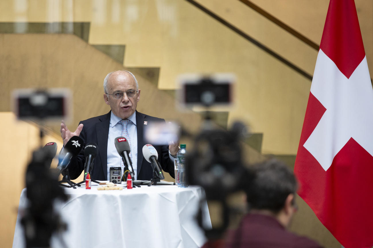 Ueli Maurer parla di fianco a una bandiera svizzera.