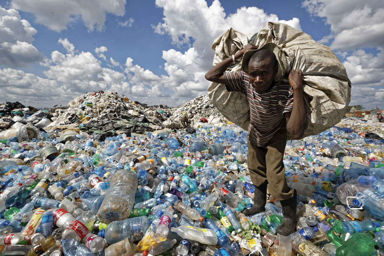 Uomo con un grande sacco sulle spalle nel mezzo di un immensa discarica.