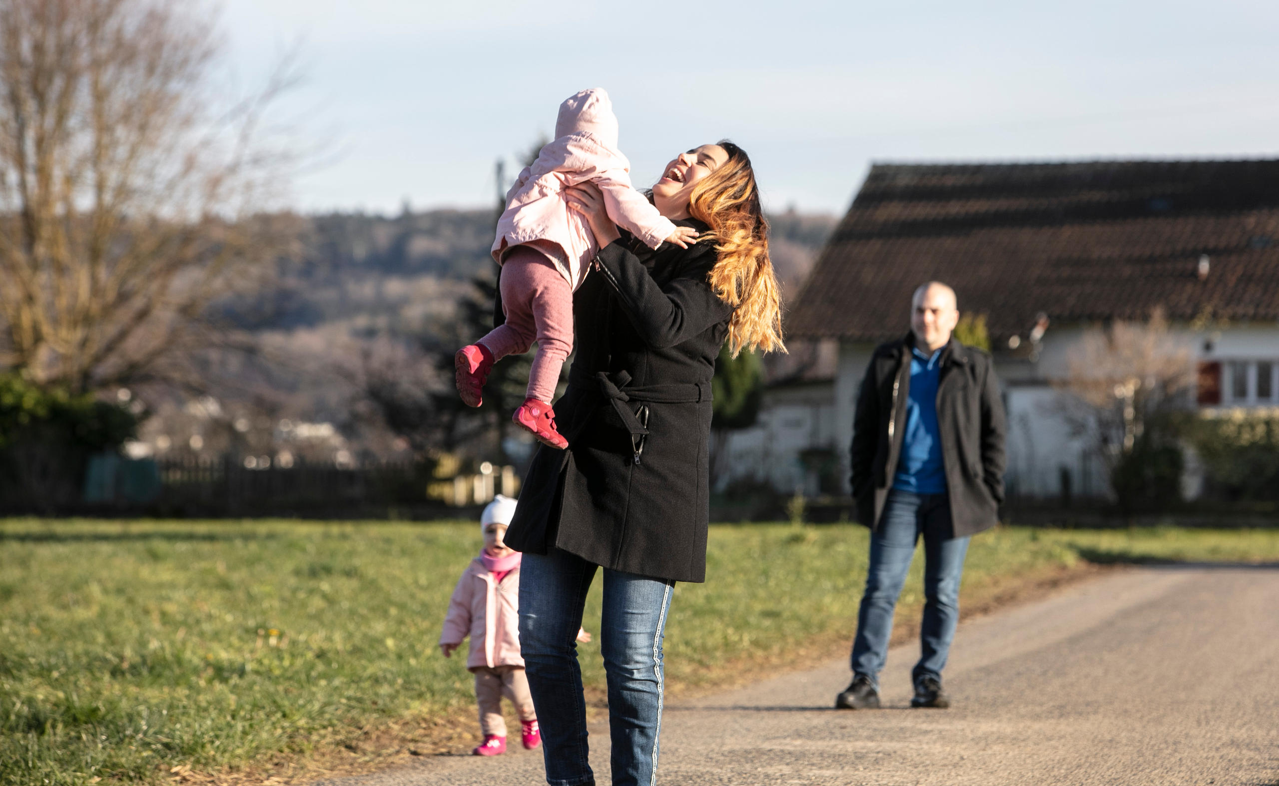 La mamma solleva una gemellina, mentre l altra e il papà restano un po indietro e le guardano.