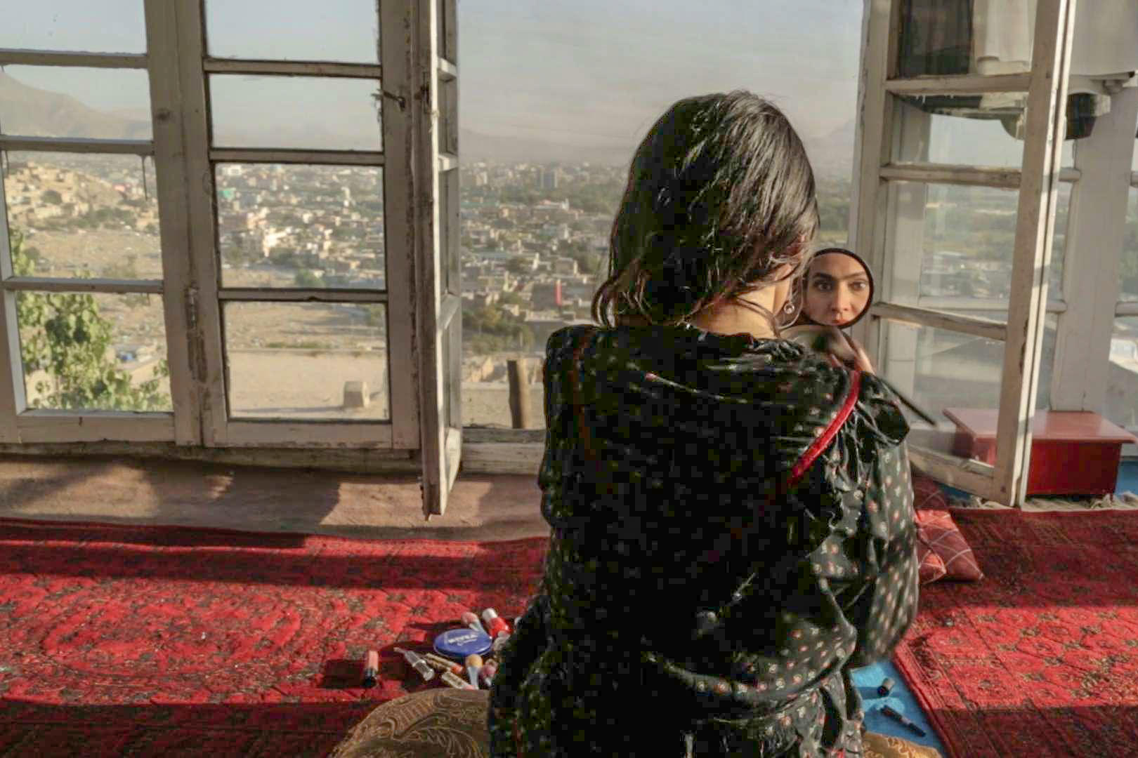 Woman sees herself on a mirror, with a city view sprawling beyond her window