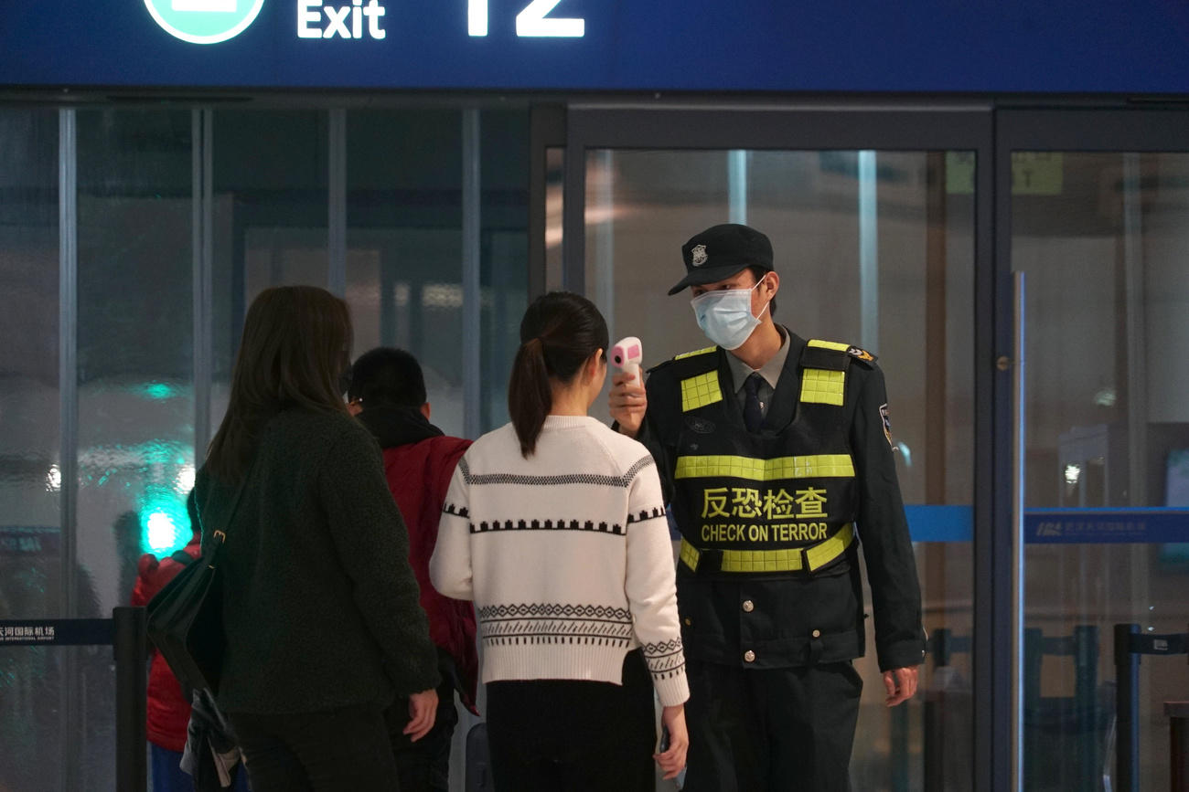 Un poliziotto con la mascherina controlla una ragazza mentre lascia l aeroporto internazionale di Wuhan.