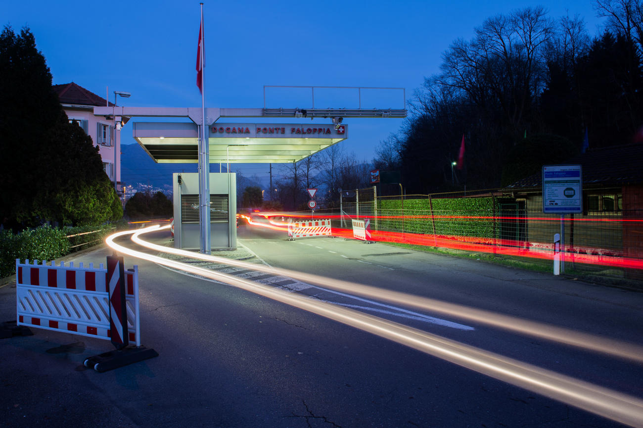 Immagine di una strada con casello/guardiola con scritta Dogana tra le corsie; scie luminose di auto di passaggio