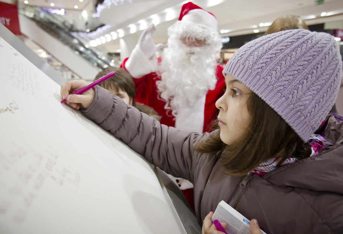 Una niña escribe en una gran hoja de papel. Junto a ella, Papá Noël.