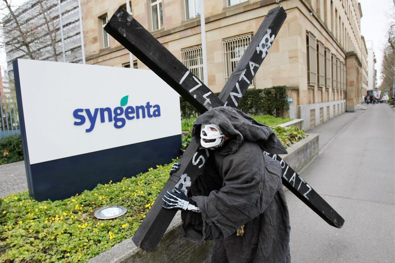 Manifestante com máscara de morte carregando uma enorme cruz negra na frente da sede da Syngenta