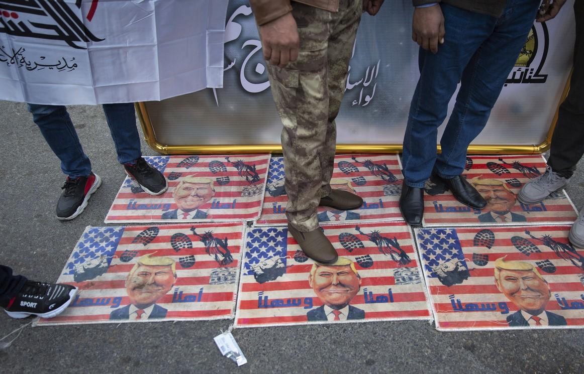 Los Manifestantes pasan por encima de una bandera estadounidense con fotos del presidente Trump