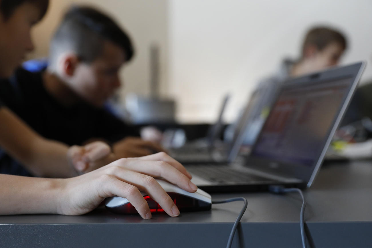 Ein Laptop auf einem Tisch, im Vordergrund eine Maus und eine Kinderhand.