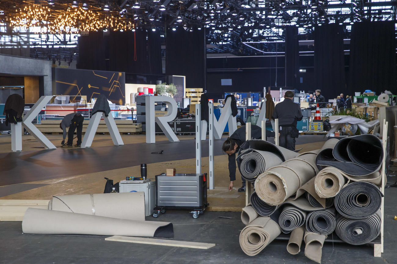 Due sportelli con scritto Caisses/Kassen e il logo Geneva Motor Show ; operai spostano un totem