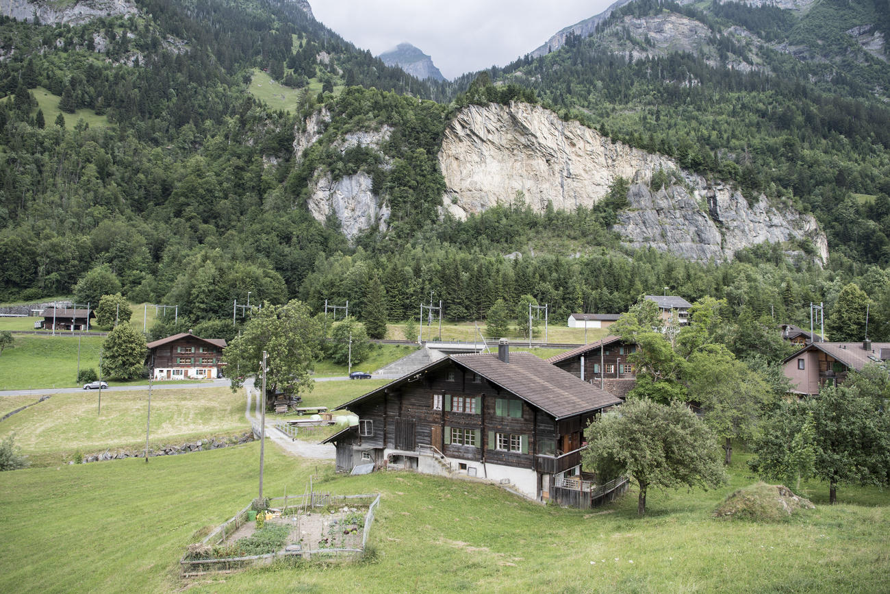 Veduta semi-aerea di una vallata; sul fondo, una frana sovrastata da un prato; a valle, strade, ferrovia e case in legno