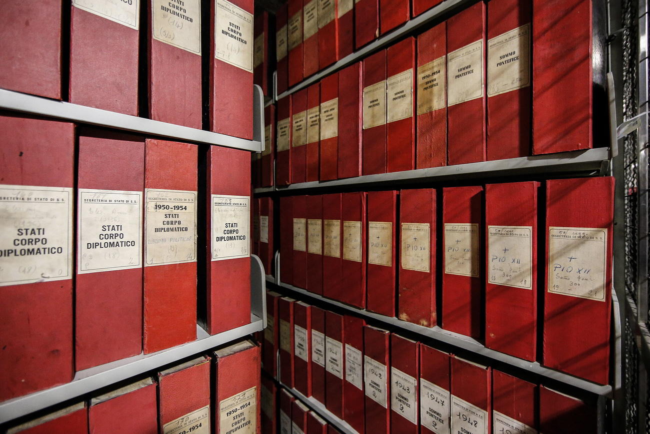 Immagine di faldoni rossi sistemati su scaffali d archivio, si intravvede la scritta Pio XII