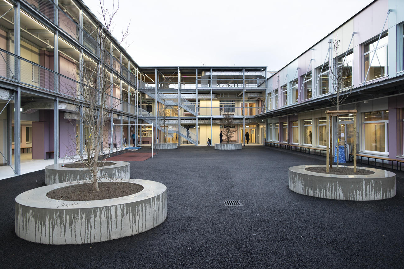 Cortile interno rettangolare di un edificio in cemento con pannelli colorati e vasche con alberi appena piantati