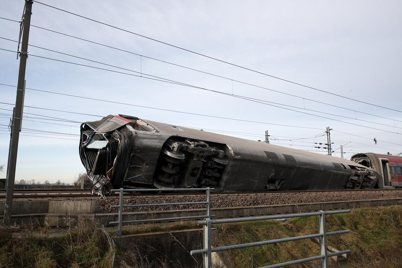 Testa di un treno, senza motrice e con prima carrozza inclinata di lato, fermo su un binario in aperta campagna
